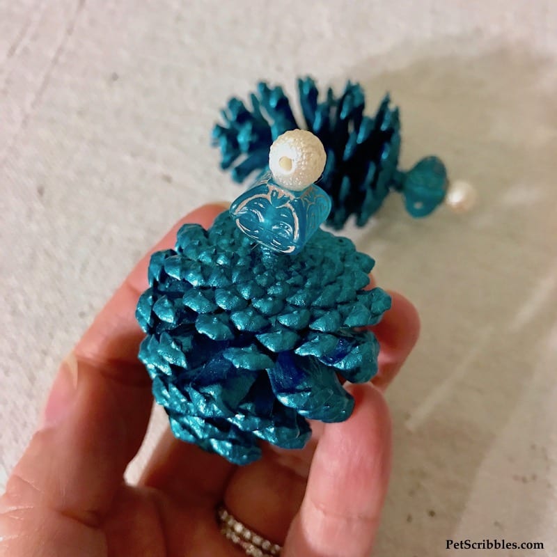 attaching beads to a painted pinecone to make an ornament