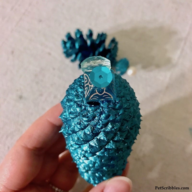 finishing touches on a teal painted pinecone ornament
