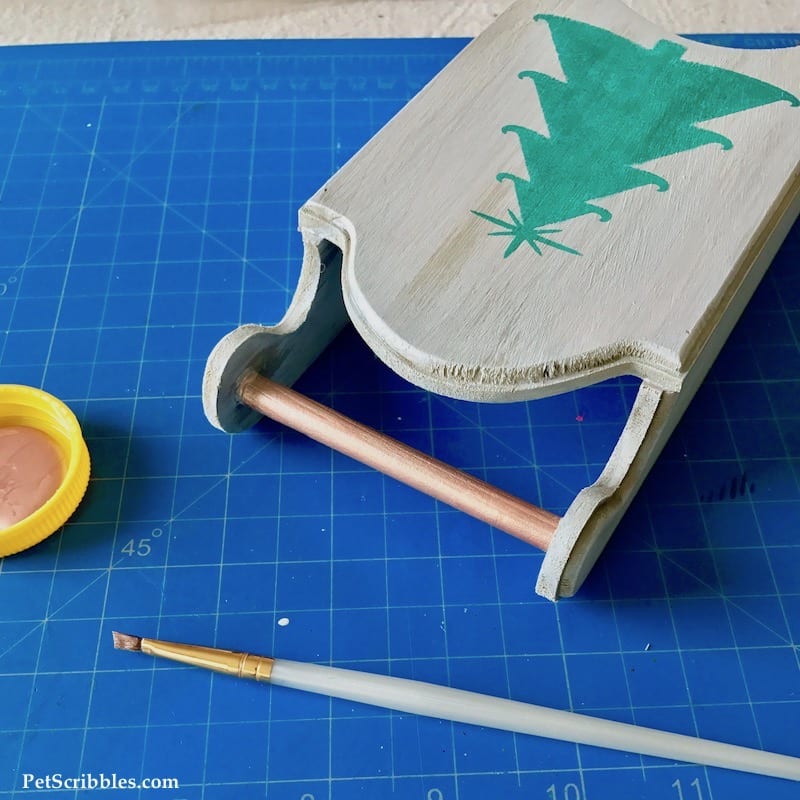 painting rose gold accents onto a wood sled decoration