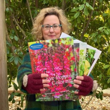 woman holding her favorite plant and seed catalogs standing outdoors with greenery behind her