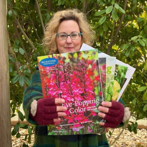 woman holding her favorite plant and seed catalogs standing outdoors with greenery behind her