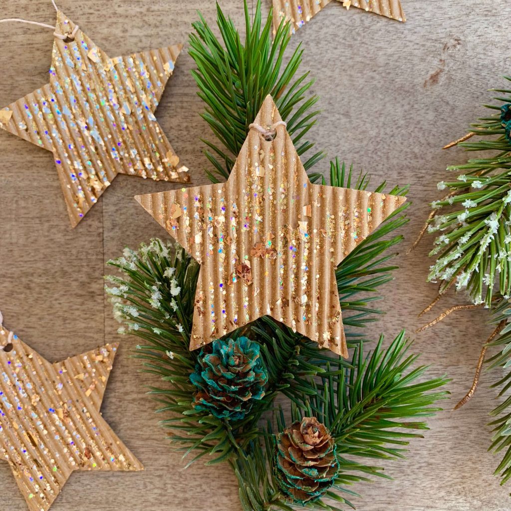 corrugated cardboard star ornaments with glitter on fake pine branch with mini pinecones